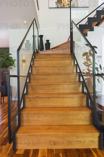 Black powder coated steel L-shaped staircase with stained and varnished wooden steps and tempered