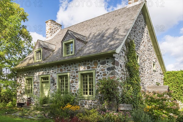 Old circa 1735 Canadiana fieldstone house facade with lime green trim and cedar wood shingles roof