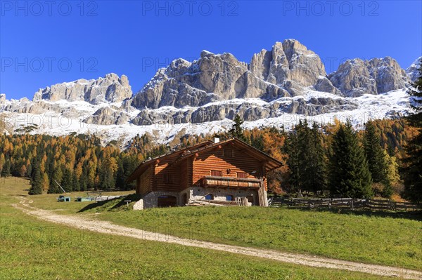 Red roof of a wooden hut in front of a wide mountain panorama under a blue sky, Italy, Alto Adige,
