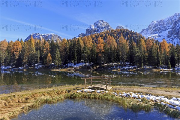Autumn mountain landscape with a bridge over a clear lake and snow-covered peaks, Italy, South