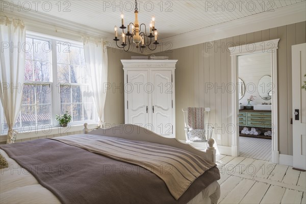 King size bed with light brown and beige striped bedspread, white painted wooden headboard and