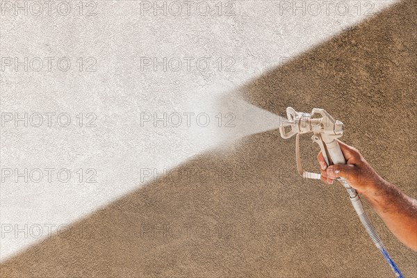 Professional spray painter holding spray gun spraying white paint over brown stucco surface