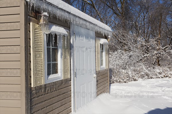 Storage shed facade covered in thick ice and snow in residential backyard after ice storm in early