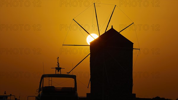 Silhouette of a windmill against the background of an orange sunrise sky, twilight, Mandraki Oat,