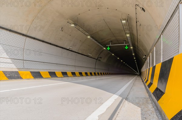 Two lane highway tunnel of white concrete with florescent lights and green arrows on ceiling and