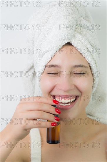 Happy young woman with towel on head holding amber glass bottle of skin serum. Beautiful young