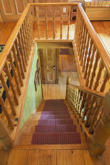 Looking down staircase with maple wood railings and pine wood steps covered with multi-coloured