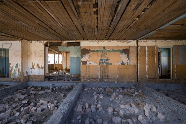 Destroyed abandoned classroom of the old school, wall painting with Soviet miners, ghost town,