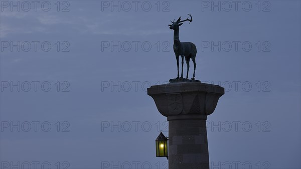 Deer statue on column with illuminated lantern at dusk, Mandraki Oat, Rhodes, Dodecanese, Greek