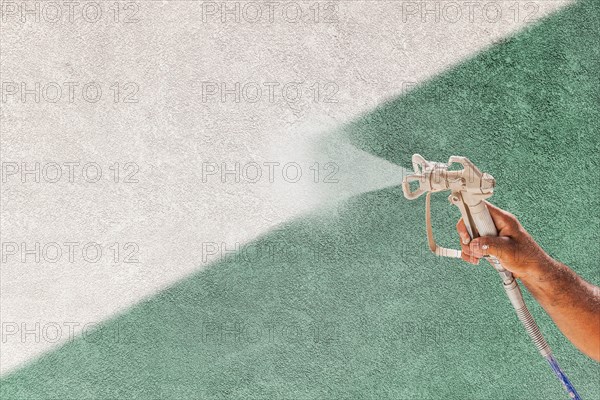 Professional spray painter holding spray gun spraying white paint over teal stucco surface