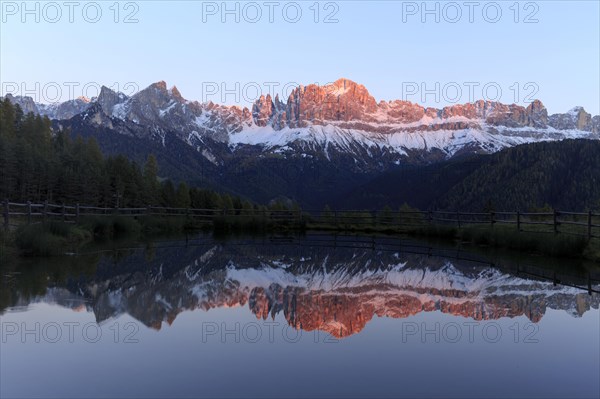 Early morning light illuminates a mountain range reflected in a still lake, Trentino-Alto Adige,