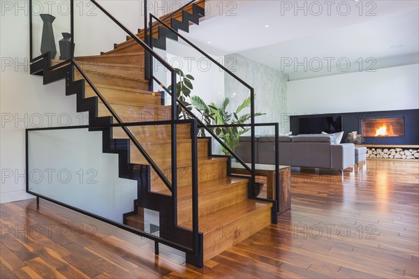Black powder coated steel L-shaped staircase with stained and varnished wooden steps and tempered