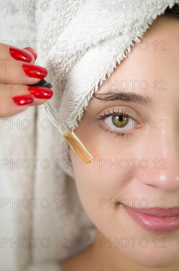 Happy young woman applying serum on her face with her eyes open. Beautiful young Brazilian woman
