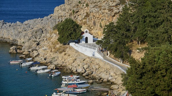 Small church on a rocky path surrounded by boats on a clear sea, St Paul's Chapel, Paul's Bay,
