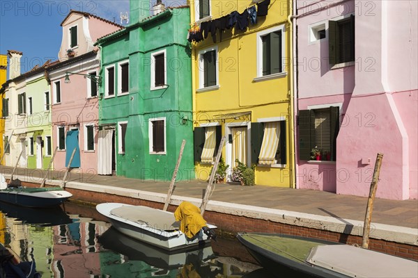 Moored boats on canal lined with pink, yellow and green stucco houses decorated with striped