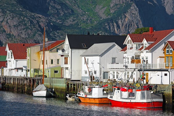 Fishing boats in front of wooden houses and high mountains in a small harbour, Idyll, Henningsvaer,