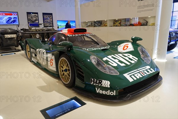 PORSCHE 911 GTI 98, front view of a green Porsche racing car with sponsor logo in a showroom,