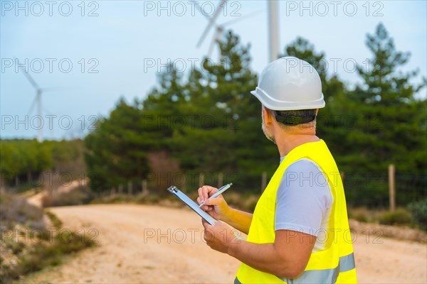 Rear view of a male mature engineer writing notes inspecting wind turbines in a green energy park