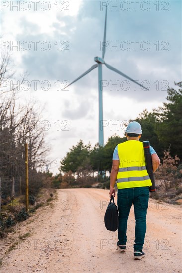 Vertical photo of the rear view of a male caucasian adult engineer walking along a path of green