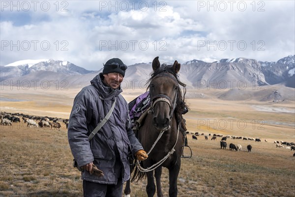 Nomadic life on a plateau, shepherd on horse, flock of sheep, dramatic high mountains, Tian Shan