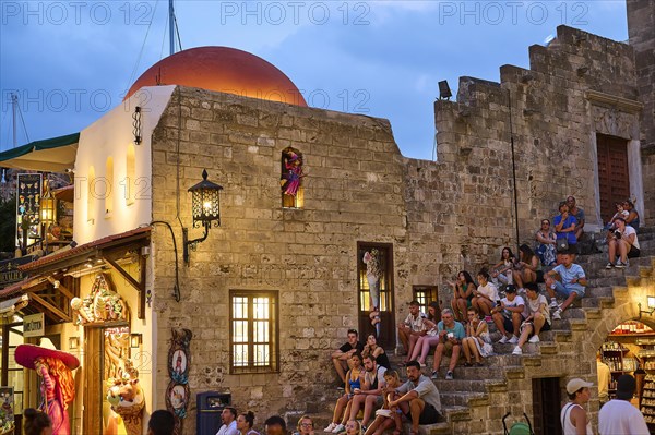 Hippocrates Square, St Paul's Gate, tourists sitting on old walls next to a white building with a