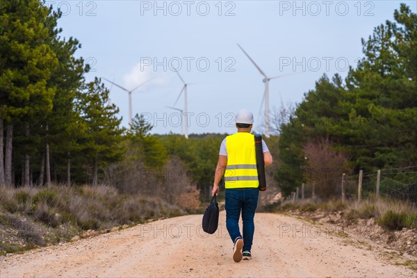 Rear view of a mature caucasian male worker walking along a path in a green energy park with wind