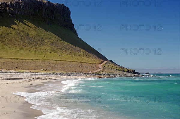 Lonely sandy beach and gravel track in front of vegetation-free mountains, Latrabjarg, Westfjords,