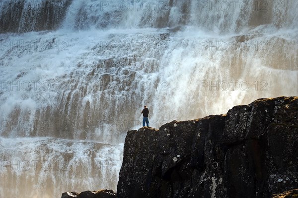 Man standing on a rock in front of the falling water of a waterfall, Dyandi, Westfjords, Iceland,