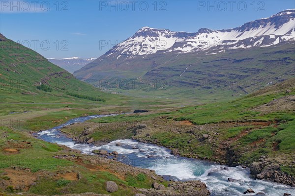 Water falls into a deeply incised valley framed by high mountains, ferry town, Seydisfjoerdur, East
