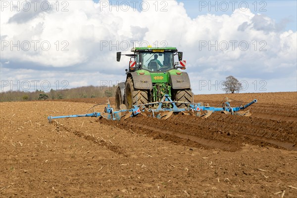 Green John Deere tractor ploughing deep furrows to prepare soil for potato crop, Ramsholt, Suffolk,