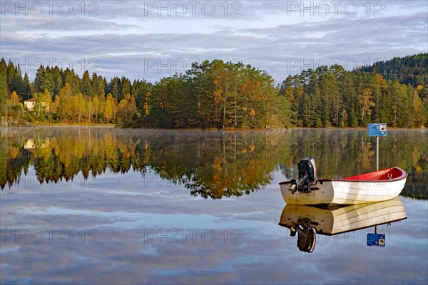 Trees and a small boat reflected in the calm waters of a lake, leaf colouring, Bullaren, Bohuslaen.