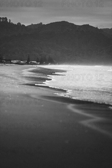 Walk on the beach at sunset, restless sea lapping waves on the beach, rocky landscape in the