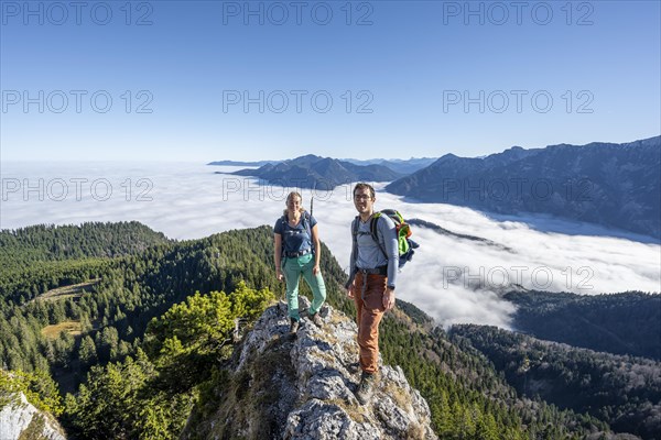 Two hikers at Ettaler Manndl, view over mountain landscape and sea of clouds, high fog in the