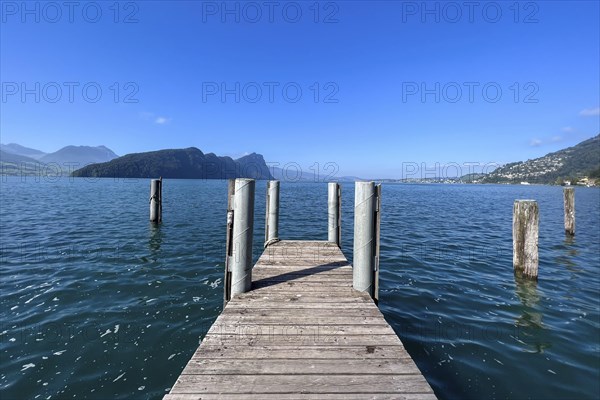 Wooden jetty juts into clear lake under blue sky, surrounded by mountains, Vitznau, Lucerne,