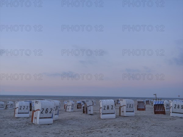 A quiet beach with white beach chairs and a gentle sunset in the sky, setting sun on a beach with
