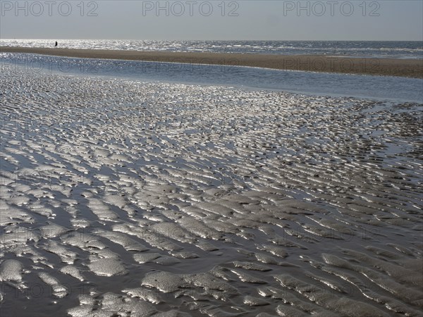 Close-up of a sandy beach with watercourse and waves in the background, glittering sea water at low