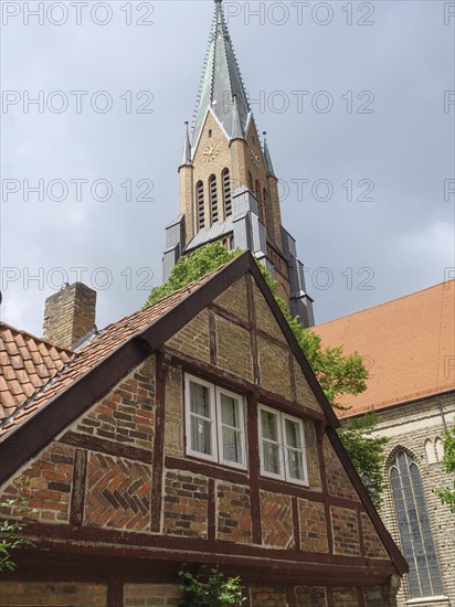 A half-timbered house in front of a high church tower, cloudy sky and a red tiled roof, large