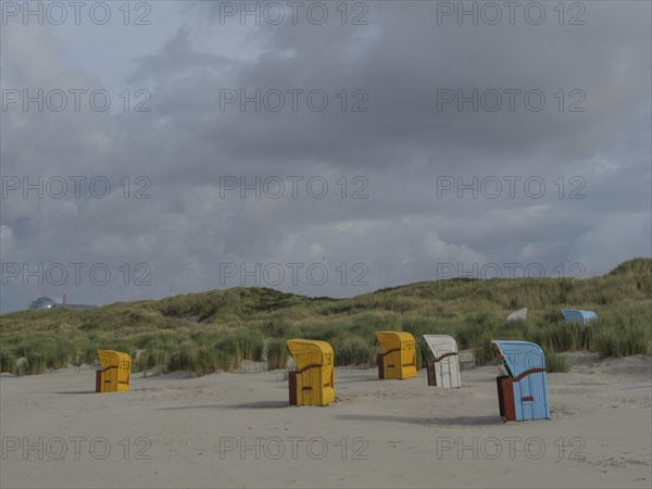 Beach chairs scattered on the beach under a cloudy sky, surrounded by gentle dunes, colourful beach