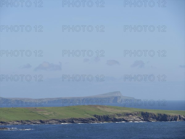Wide green fields meet the deep blue sea, with a visible island in the background, green meadows on