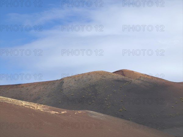 Dry, hilly desert area under a blue sky with white clouds, barren landscape of lava mountains,