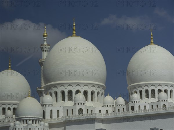 Detailed view of the white domes of a mosque with golden spires against a blue sky, large mosque