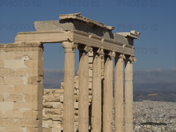 Ancient marble columns with a cityscape and mountains in the background under a clear sky,