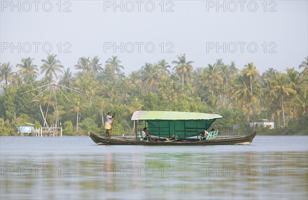 Indian man stakes his boat over the Cherai lagoon, behind blurred Chinese fishing net, Vypin