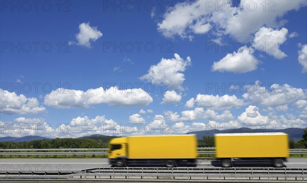 A yellow lorry drives on the A3 motorway under a blue sky with white clouds, motion blur, Bavarian