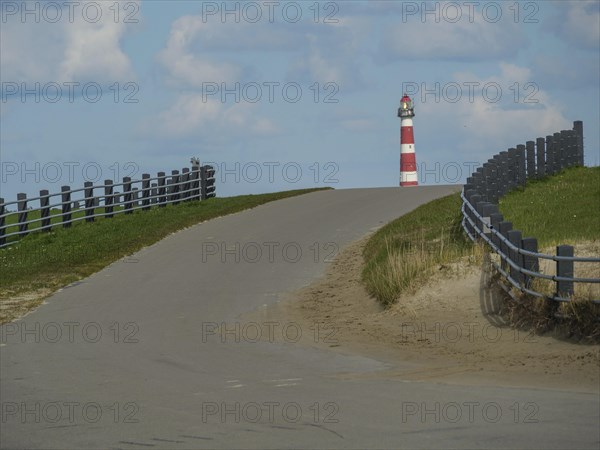 Road leads slightly uphill to a lighthouse, flanked by fences, with cloudy sky, red and white