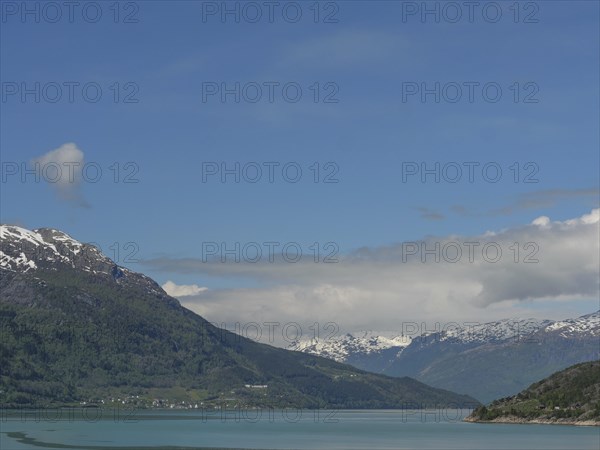 Calm waters with snow-capped mountains under a clear blue sky, greenish shimmering water in a fjord