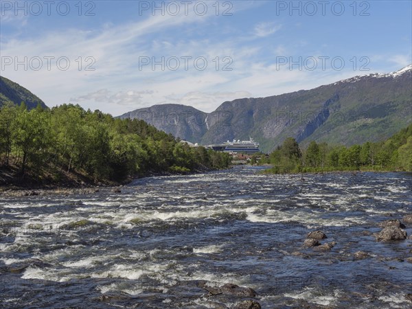 A river in a valley, surrounded by green forests and mountains, in the background a large ship,