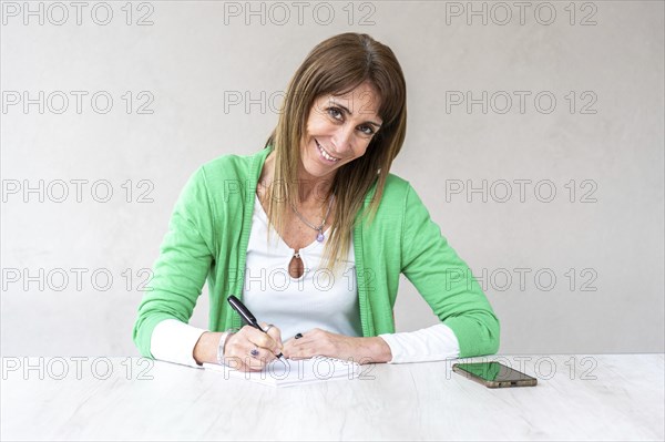 Portrait of a smiling mid-adult woman looking at the camera while she writes