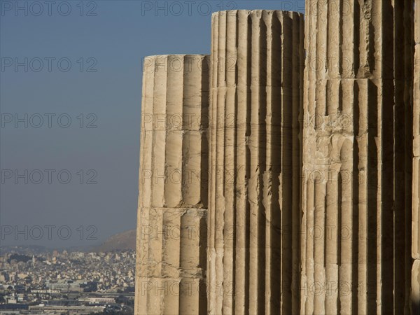 Close-up of ancient marble columns in front of a cityscape with clear sky, historical columns and