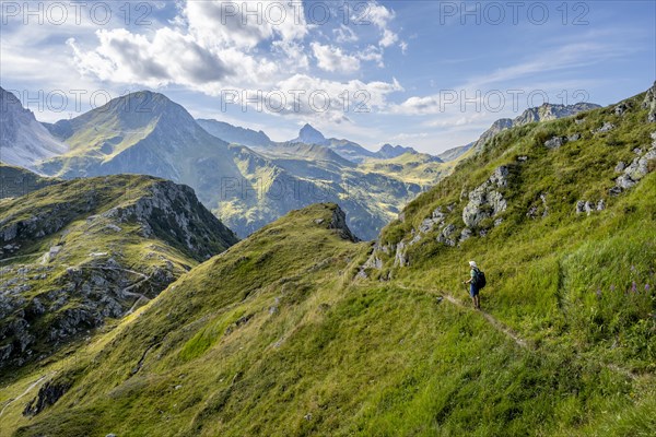 Mountaineer on a hiking trail on a grassy mountain ridge, idyllic mountain landscape with green